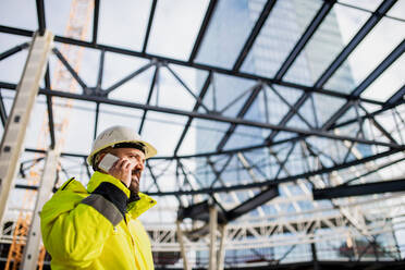 Mature man engineer standing on construction site, using smartphone. - HPIF15642