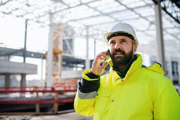 Mature man engineer standing on construction site, using smartphone. - HPIF15643