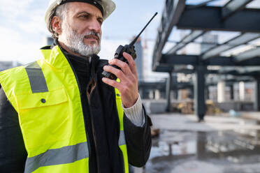 Ein Ingenieur benutzt ein Walkie-Talkie im Freien auf einer Baustelle. - HPIF15654