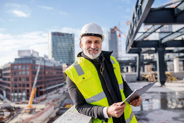 Ein männlicher Ingenieur steht im Freien auf einer Baustelle und schaut in die Kamera. - HPIF15656