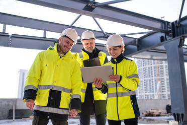 Eine Gruppe von Ingenieuren steht im Freien auf einer Baustelle und verwendet ein Tablet. - HPIF15658