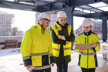 Eine Gruppe von Ingenieuren steht im Freien auf einer Baustelle und verwendet ein Tablet. - HPIF15659