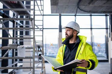 Mature man engineer standing on construction site, holding blueprints. - HPIF15668