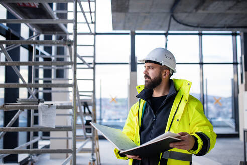 Älterer Mann, Ingenieur, steht auf einer Baustelle und hält Baupläne. - HPIF15668