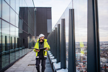 Älterer Mann, Ingenieur, der auf einer Baustelle spazieren geht und Baupläne hält. - HPIF15674