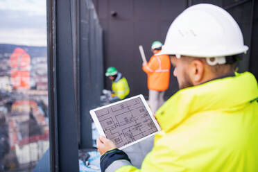 Mature man engineer standing on construction site, holding tablet with blueprints. - HPIF15677