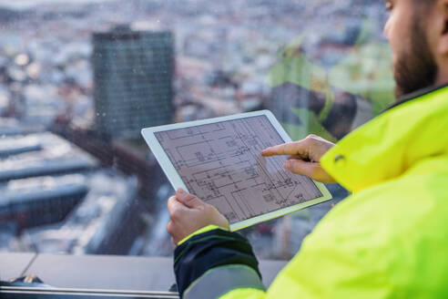 Mittelteil eines nicht erkennbaren männlichen Ingenieurs mit Tablet auf einer Baustelle, der Baupläne betrachtet. - HPIF15680
