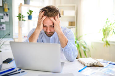 Frustrated and disappointed mature businessman with laptop indoors in home office, working. - HPIF15690