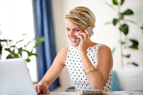 Fröhliche junge Geschäftsfrau mit Laptop und Telefon in einem Büro zu Hause bei der Arbeit. - HPIF15698