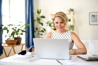 Front view of cheerful young businesswoman with laptop indoors in home office, working. - HPIF15702