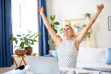 Cheerful young businesswoman with laptop indoors in home office, stretching arms when working. - HPIF15703