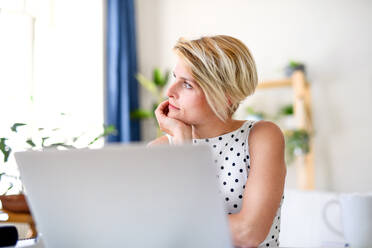 Traurige und müde junge Geschäftsfrau mit Laptop drinnen im Büro zu Hause, arbeiten. - HPIF15704