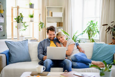 Vorderansicht eines verliebten Paares, das in einem Haus sitzt und einen Laptop benutzt. - HPIF15717