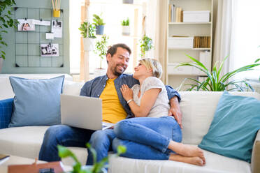 Front view of happy couple in love sitting indoors at home, using laptop. - HPIF15718