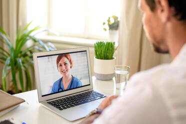 Mature man having video call with doctor on laptop at home, online consultation concept. - HPIF15743