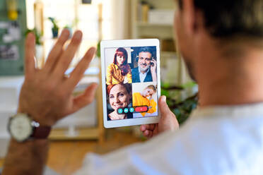 Rear view of unrecognizable man having video call on tablet at home, waving. - HPIF15749