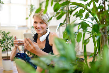 Front view of young sports woman with smartphone indoors at home, resting. Copy space. - HPIF15758