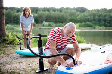 Aktives älteres Paar, das sich im Sommer am See zum Paddelboarding bereit macht. - HPIF15760