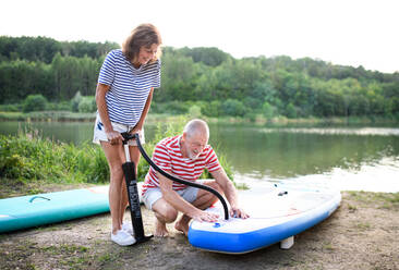 Aktives älteres Paar, das sich im Sommer am See zum Paddelboarding bereit macht. - HPIF15761