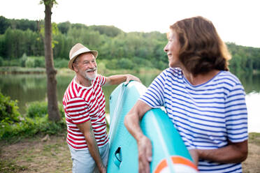Porträt eines älteren Mannes, der im Sommer ein Paddelbrett am See trägt und sich unterhält. - HPIF15764