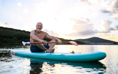 Vorderansicht eines älteren Mannes, der auf einem Paddelbrett auf einem See im Sommer sitzt, Kopierraum. - HPIF15789