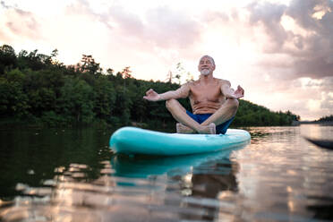 Älterer Mann auf einem Paddelbrett auf einem See im Sommer, macht Yoga-Meditationsübungen. - HPIF15799