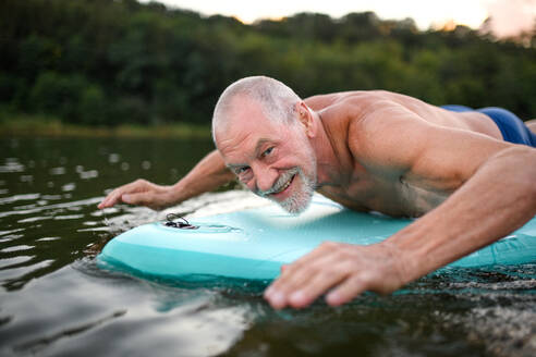 Aktiver älterer Mann auf Paddleboard auf einem See im Sommer, schwimmend. - HPIF15800