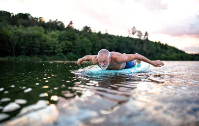 Active senior man on paddleboard on lake in summer, swimming. - HPIF15801