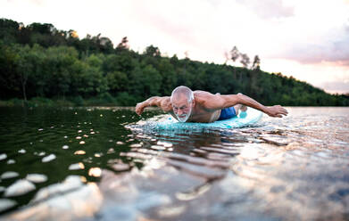 Aktiver älterer Mann auf Paddleboard auf einem See im Sommer, schwimmend. - HPIF15801