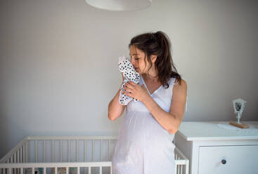 Porträt einer schwangeren Frau, die einen Mädchenbodysuit in der Hand hält, in der Vorderansicht. - HPIF15810