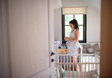 Schwangere Frau im Schlafzimmer zu Hause, die Kleidung in die Schublade legt. - HPIF15812
