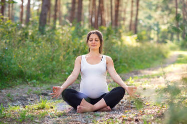 Frontansicht Porträt der glücklichen schwangeren Frau im Freien in der Natur, tun Yoga-Übung. - HPIF15826
