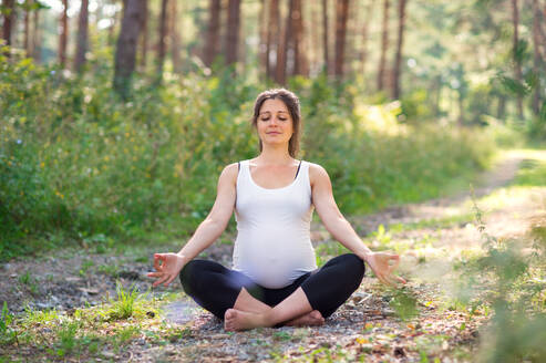 Frontansicht Porträt der glücklichen schwangeren Frau im Freien in der Natur, tun Yoga-Übung. - HPIF15826