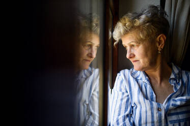 Traurige ältere Frau, die zu Hause am Fenster steht, Koronavirus und Quarantänekonzept. Raum kopieren. - HPIF15842