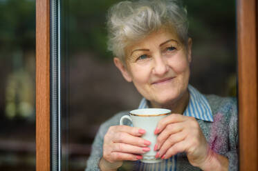 Traurige ältere Frau mit Kaffee, die zu Hause nach draußen schaut, Corona-Virus und Quarantänekonzept. - HPIF15845