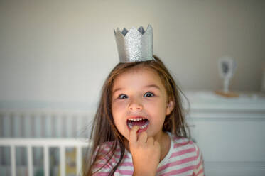 Portrait of happy small girl with princess crown on head indoors, looking at camera. - HPIF15858
