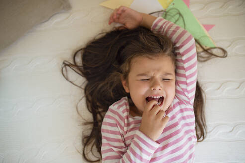 Draufsicht auf ein unglückliches kleines Mädchen, das weinend auf einem Bett liegt. - HPIF15878