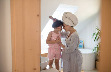 Seitenansicht Porträt der schwangeren Frau mit kleiner Tochter drinnen im Bad zu Hause, Bürsten der Haare. - HPIF15895