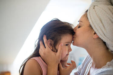 Portrait of mother kissing small daughter indoors in bathroom at home. - HPIF15896