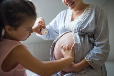 Kleines Mädchen, das den Bauch einer nicht erkennbaren schwangeren Mutter im heimischen Badezimmer eincremt. - HPIF15899