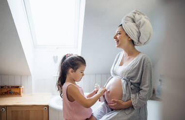 Glückliches kleines Mädchen creaming Bauch der schwangeren Mutter drinnen im Bad zu Hause. - HPIF15901