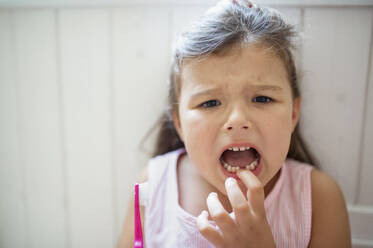 Front view portrait of worried small girl with toothbrush indoors, loosing baby tooth. - HPIF15909