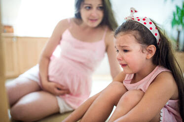 Portrait of pregnant woman with crying small daughter indoors at home, sitting. - HPIF15921