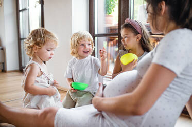 Happy pregnant woman with small children indoors at home, eating biscuits. - HPIF15937