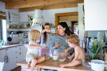 Glückliche schwangere Frau mit drei kleinen Kindern zu Hause bei der Zubereitung des Frühstücks. - HPIF15941