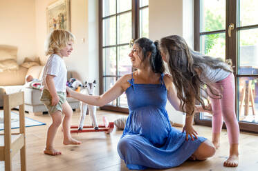 Glückliche schwangere Frau mit kleinen Kindern, die zu Hause spielen. - HPIF15949