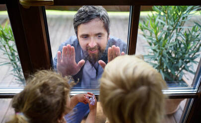 Doctor coming to see and greet children in isolation, window glass separating them. - HPIF15976