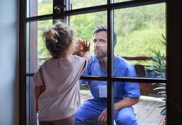 Der Arzt kommt, um die Familie in der Isolation zu sehen und zu begrüßen, das Fensterglas trennt sie. - HPIF15979