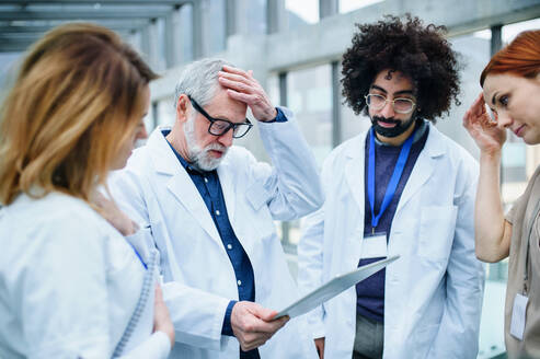 Eine Gruppe von besorgten Ärzten mit einem Tablet auf einer Konferenz, ein medizinisches Team, das Probleme diskutiert. - HPIF16115