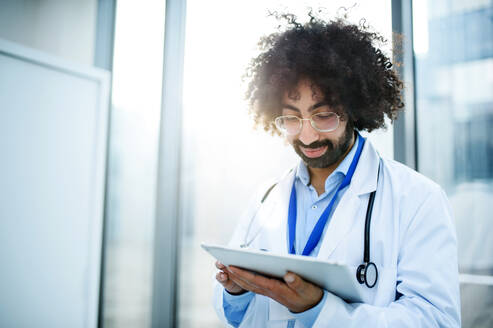 Porträt eines männlichen Arztes, der im Krankenhaus steht und ein Tablet benutzt, Kopierraum. - HPIF16128